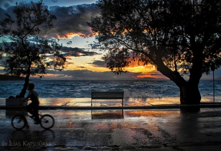 A boy with a bicycle and a sunset with clouds and reflections